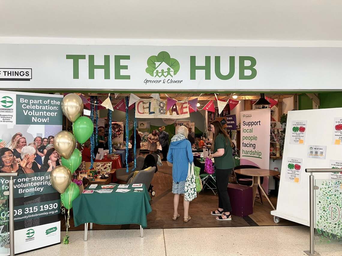 People standing at entrance to the Hub from Greener & Cleaner in the Glades Bromley. Tall signs about volunteering on at the entrance to and inside the Hub